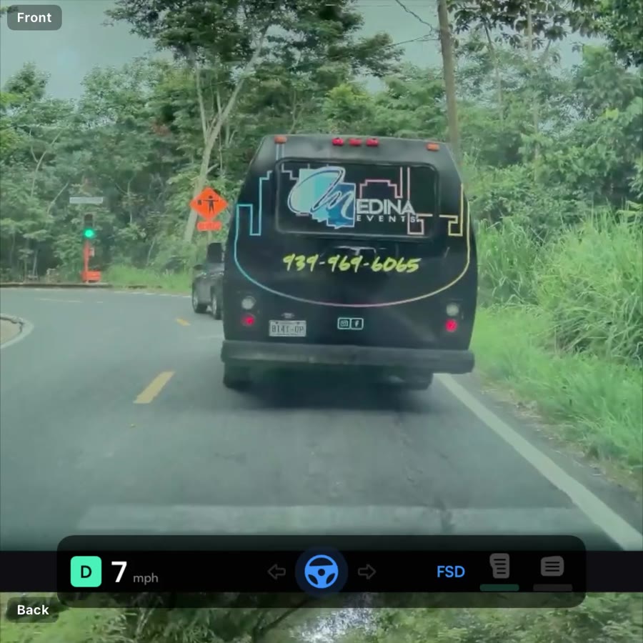 Vista del dashcam frontal: Tesla siguiendo un bus en carretera rural de Orocovis, vegetación tropical a ambos lados